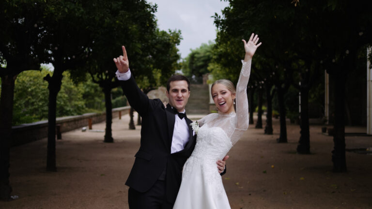 Foto espontánea de boda en Hotel Miramar: pareja feliz celebrando entre árboles, vestidos de blanco y negro clásico.